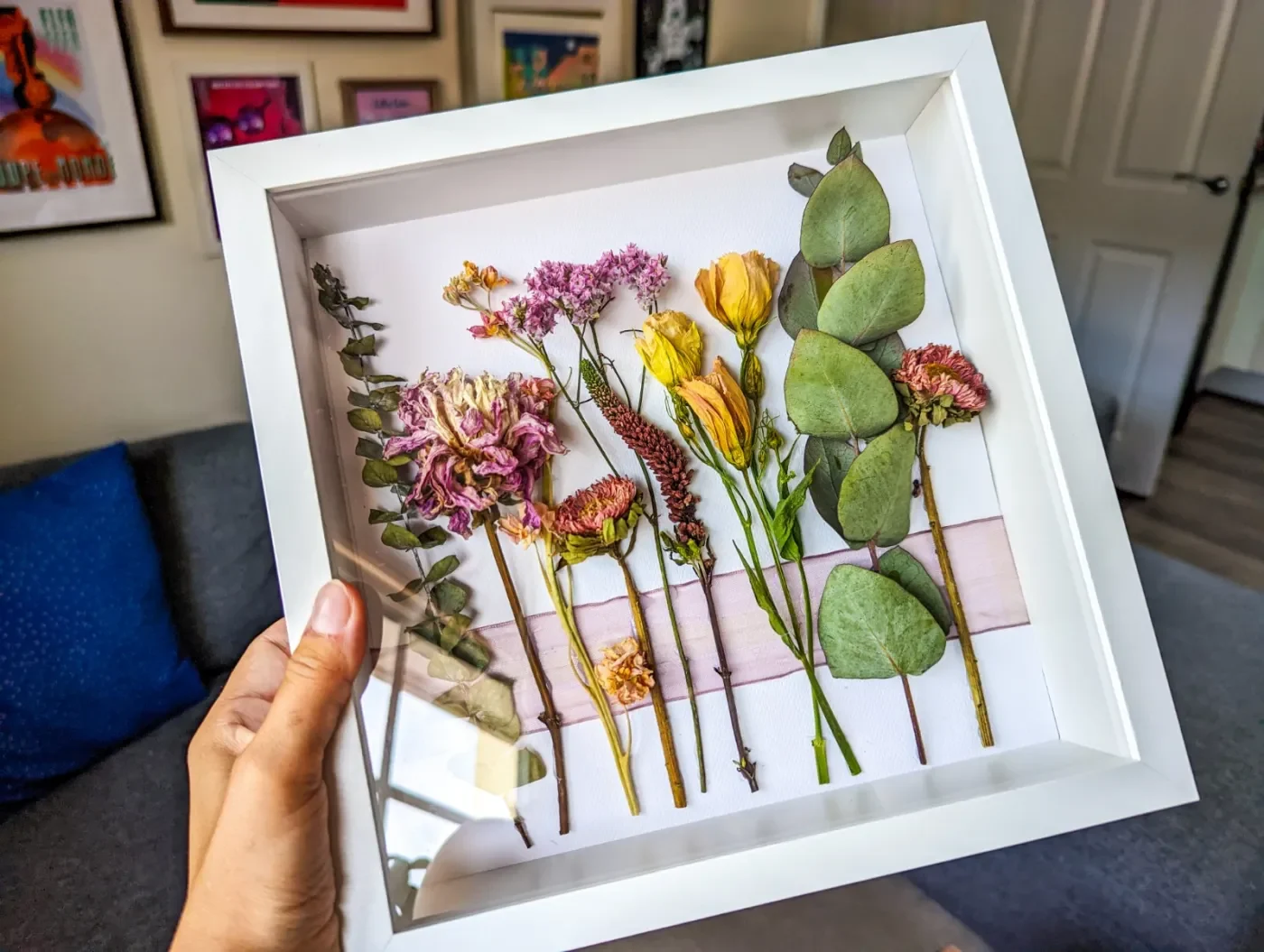 A beautifully crafted floral shadow box featuring delicate flowers arranged creatively, perfect for enhancing wedding reception decorations on a budget. The shadow box showcases a mix of vibrant blooms, adding elegance and charm to any event setting.