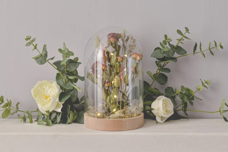 A stylish glass dome display featuring elegant floral arrangements, perfect for wedding reception decorations on a budget. The dome enhances the beauty of the setting while adding a touch of sophistication.